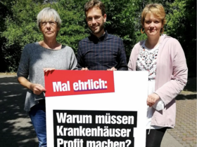 Ruth Rogée, Tobias Bank und Marianne Esders halten ein Plakat mit der Frage: "Warumm müssen Krankenhäuser Profit machen?" 
